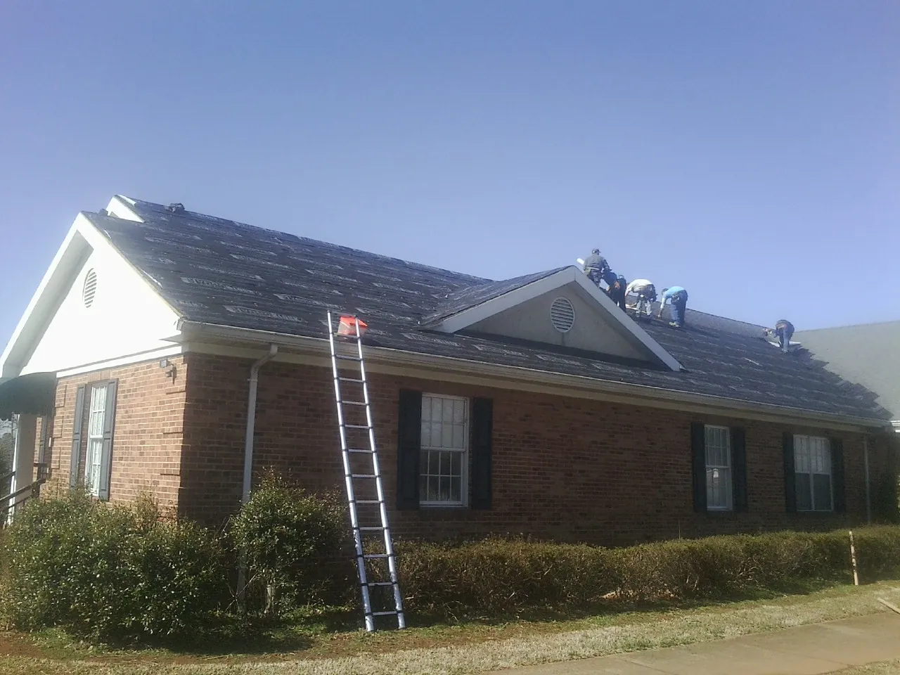 Crew tearing shingles off a brick ranch roof with a ladder set — Emergency Roof Repair work by our crew in Gilbertsville