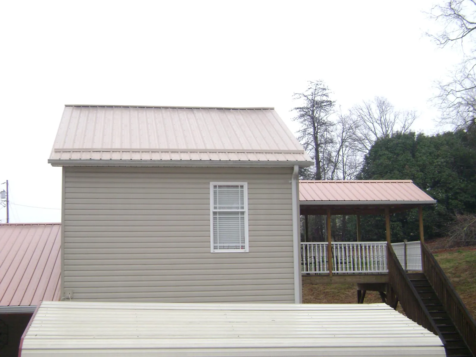 Tan metal roofs on a two story addition and attached porch, from a Roof Replacement job in Gilbertsville